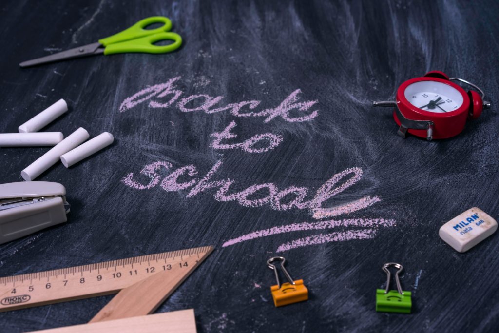 "Back to School" written on a chalkboard littered with rulers, paperclips and other school supplies.