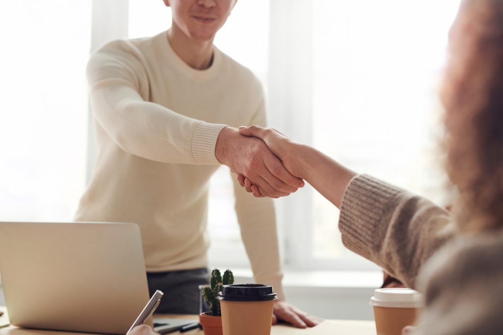 Two people shake hands over a table during a job interview.