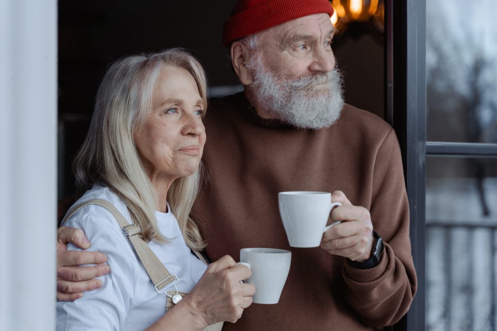 A man and a woman holding coffee cups standing in a doorway and looking outside.