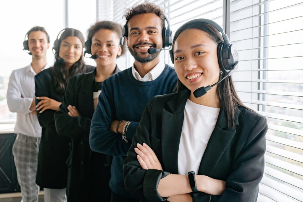 Five smiling professionals with headsets stand in a staggered line ready to help clients.