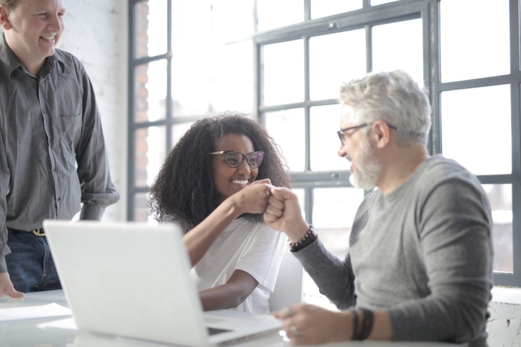 Two people sitting at a table fist-bumping in front of an open laptop.