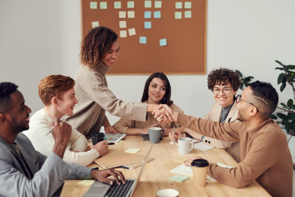 Six business professionals sitting around a conference table smiling. Two people are shaking hands.