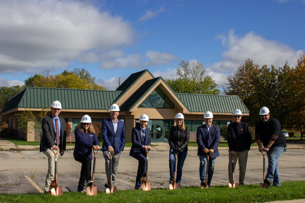 Eight members of the Consumers team standing on the site of its first Lansing office.