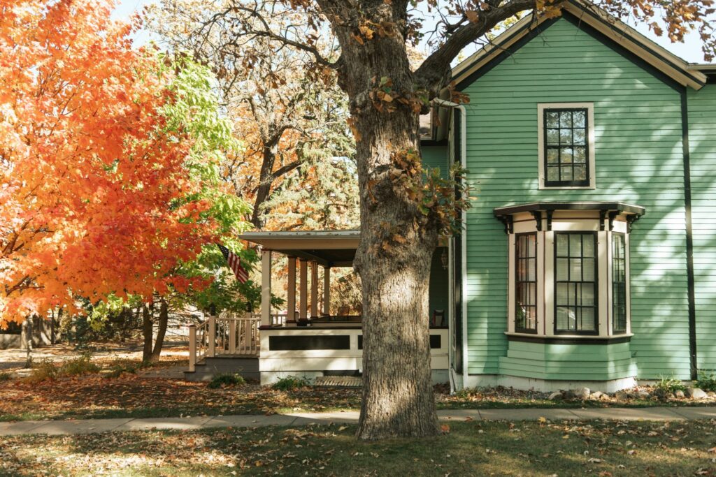 A green house sitting on a block surrounded by fall-colored trees.