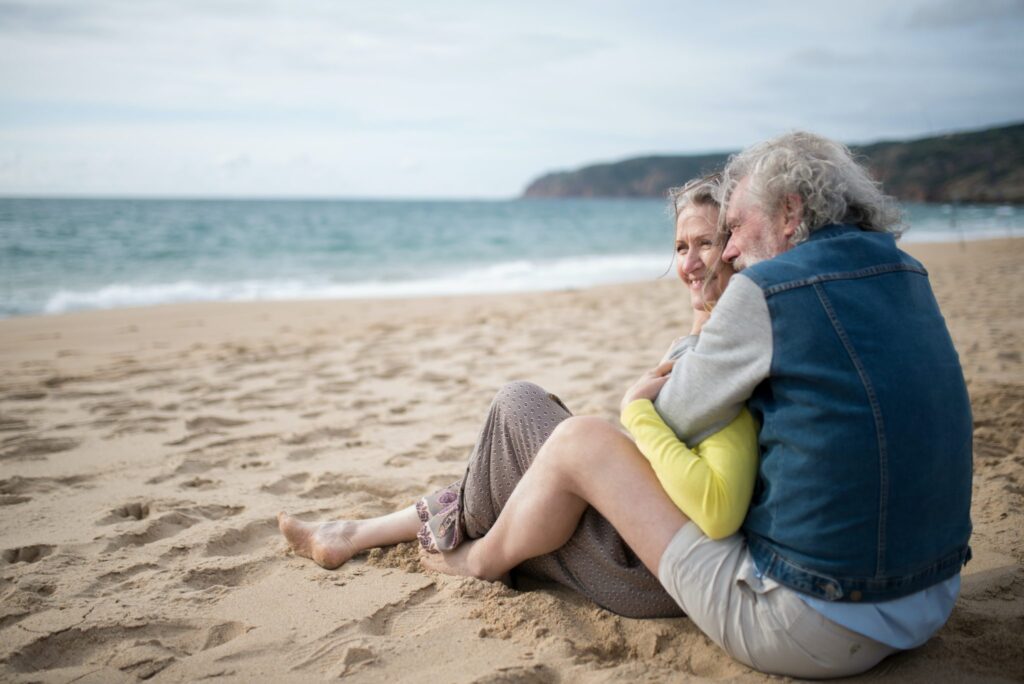 A couple sitting together on a beach as they look out toward the waves.