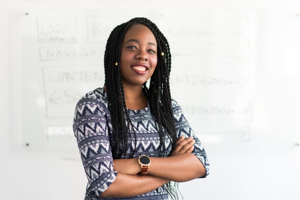 A confident woman standing with her arms crossed in front of a whiteboard.