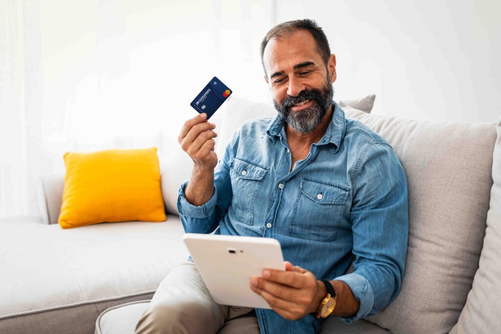 Man smiling and looking at his tablet while holding a Consumers Cash Back credit card