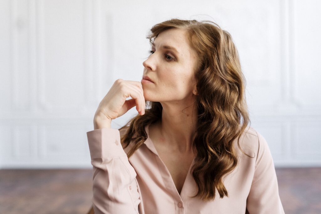 A woman in professional business attire resting her head on her fist as she gazes contemplatively into the distance.