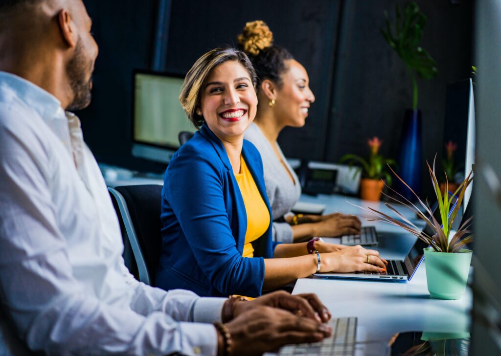 A smiling woman sitting at a table in front of an open laptop smiling at the man seated next to her.