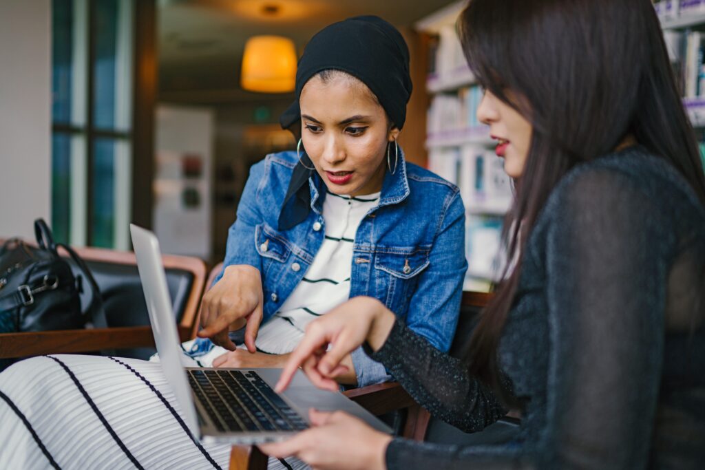 Two business women sitting on a bench collaborating over an open computer.