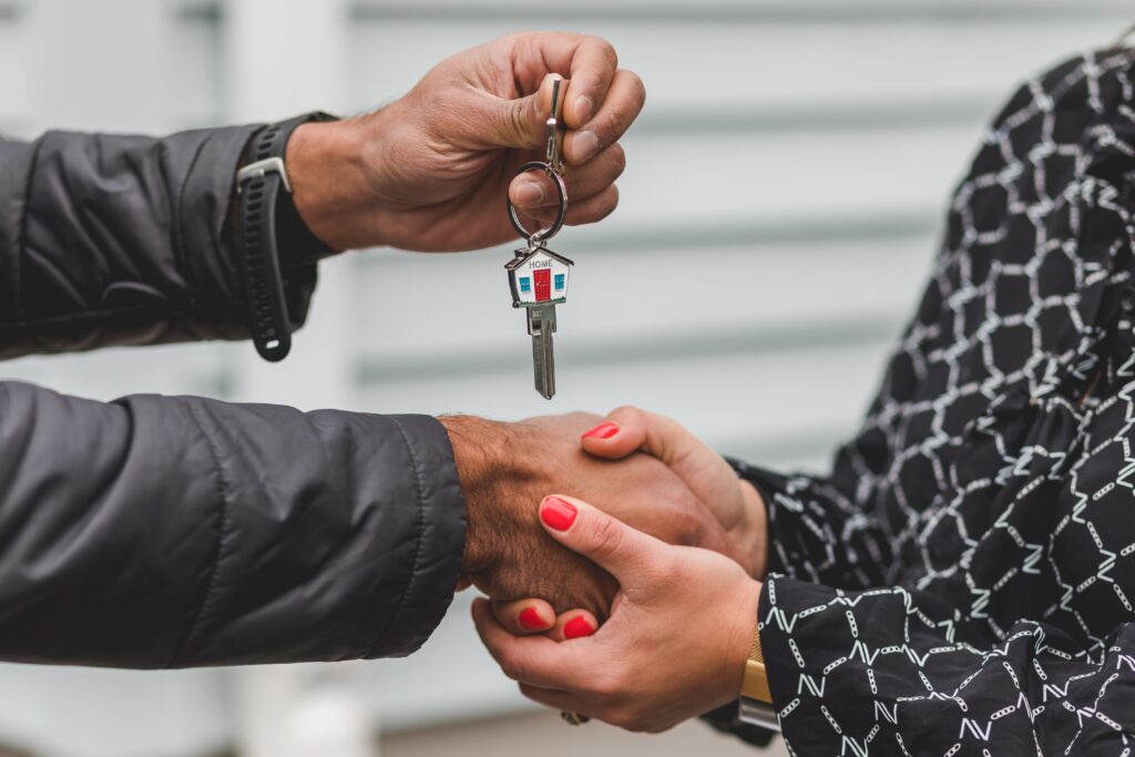 A man and woman shaking hands beneath another hand holding a house key.
