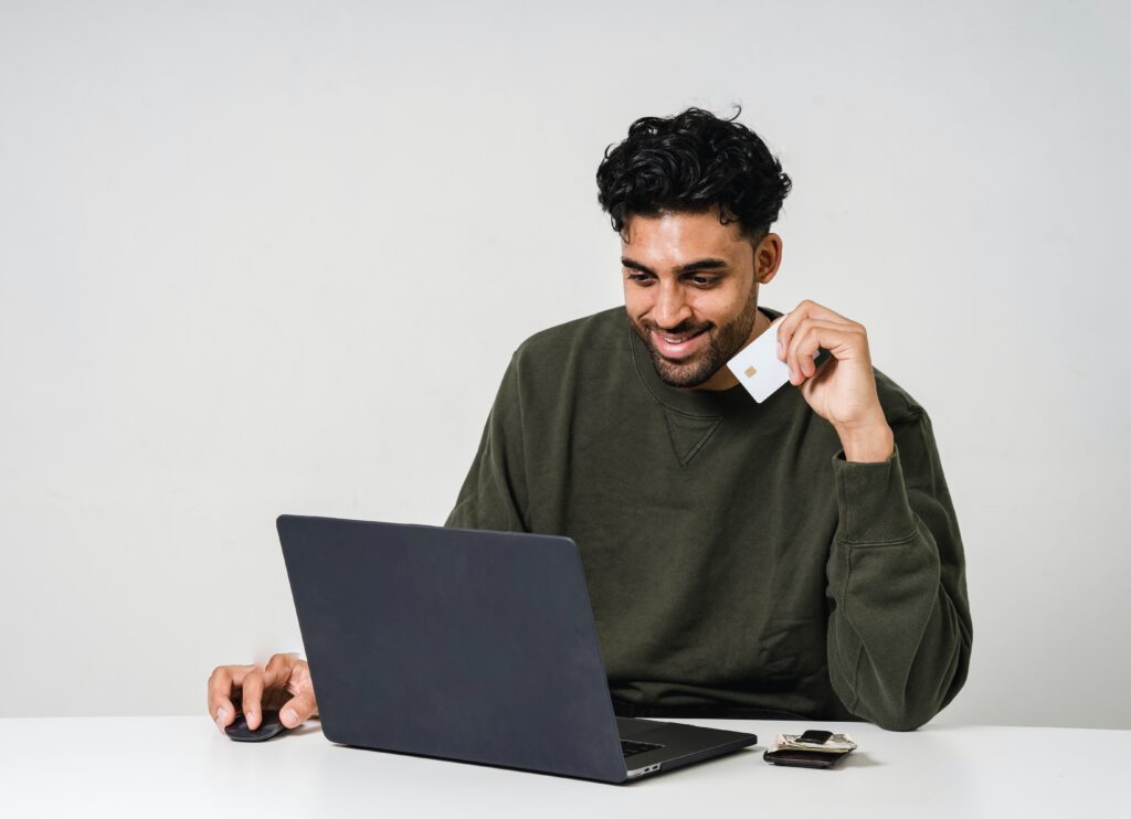 A man smiling at his computer screen as he holds his credit card.