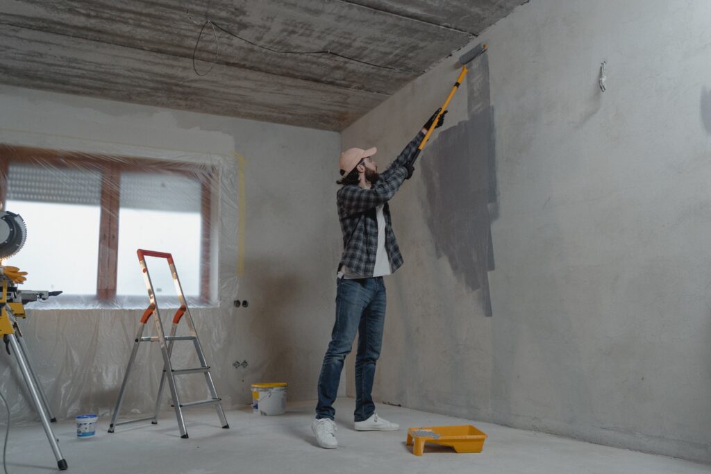 A man wearing safety equipment painting a wall in an empty room.