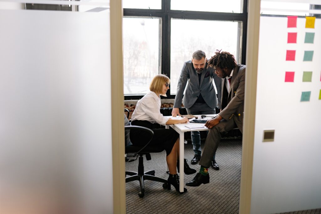 Three professionals are leaning over a desk as they collaborate.
