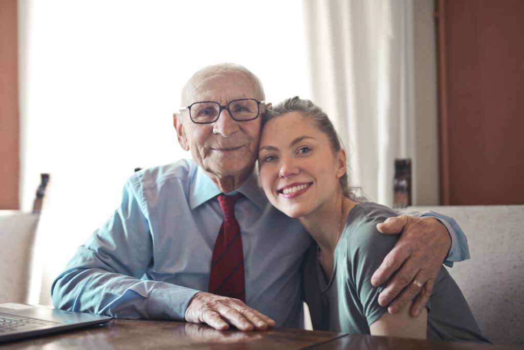 An older man embraces his granddaughter while they sit at a table.