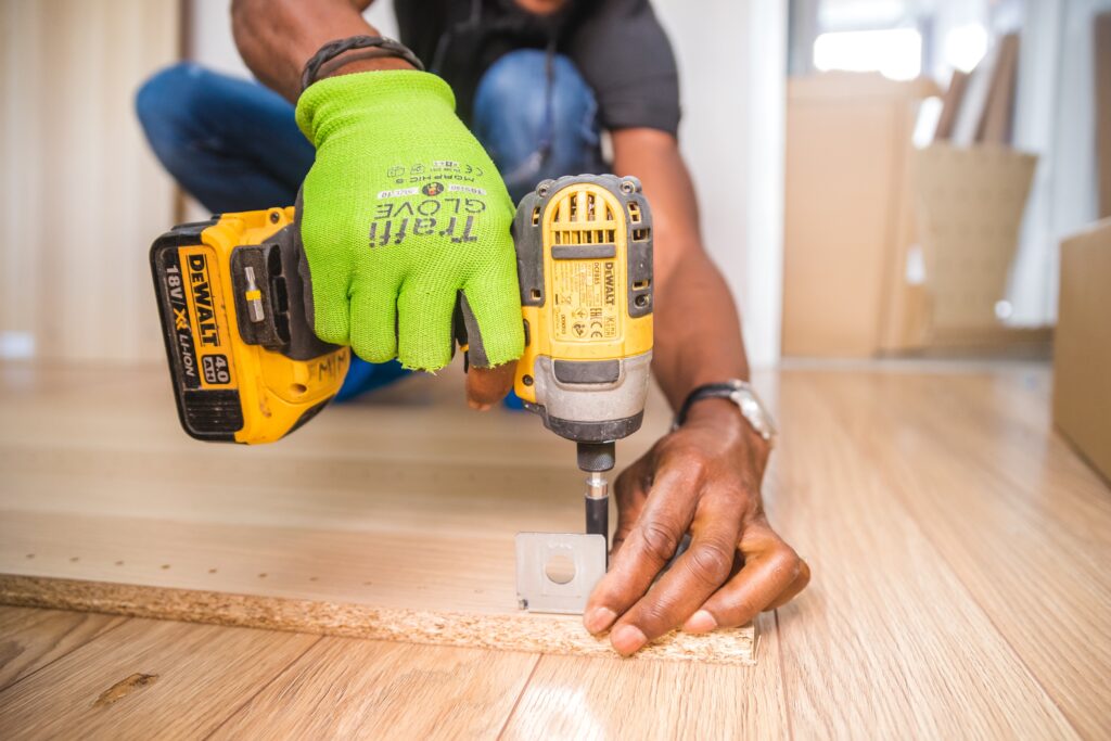 A person wearing green gloves uses a power drill.