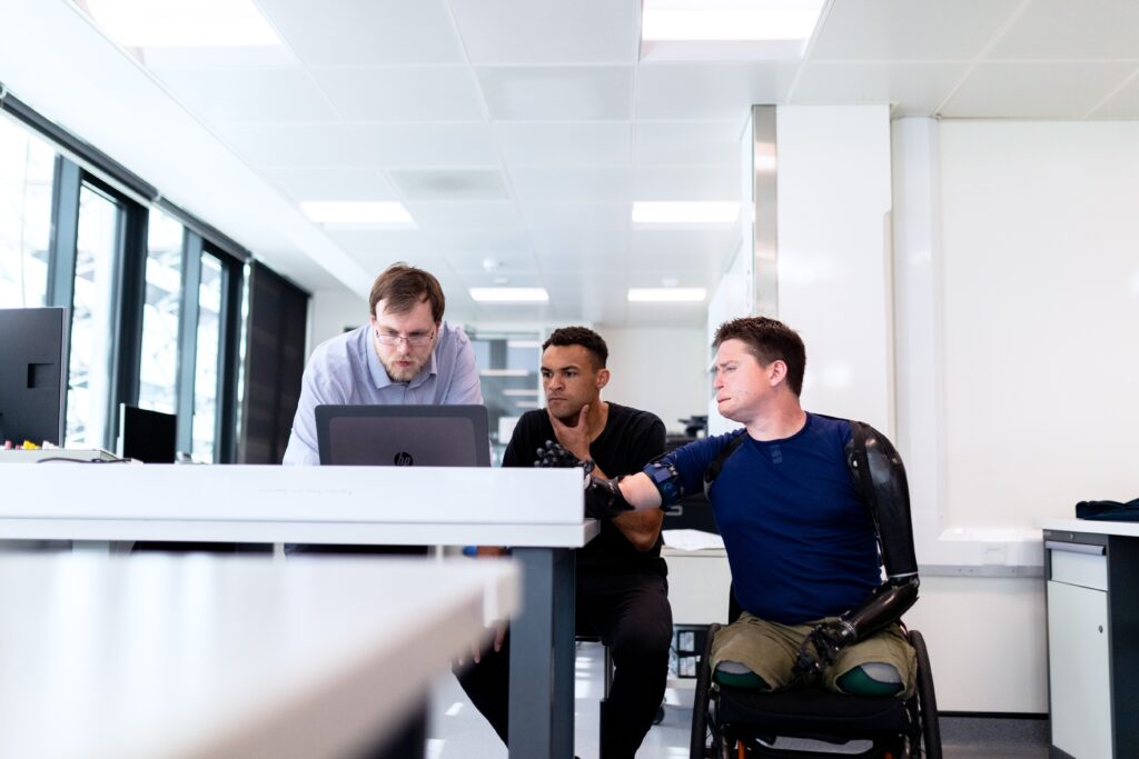 Three people peer at a computer screen in an office.