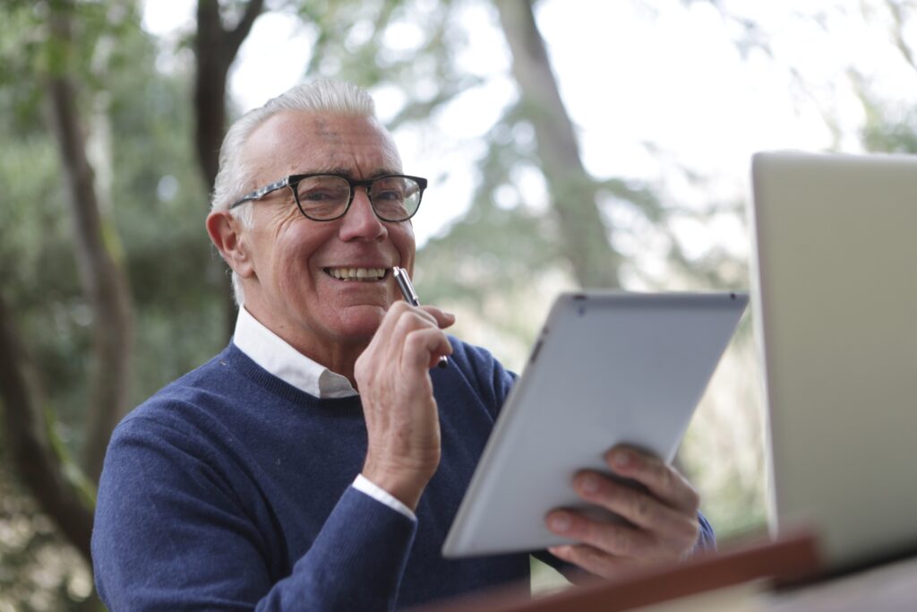 A man with white hair and glasses smiles as he reviews a document.