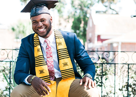 Black male graduate sitting on bench and smiling