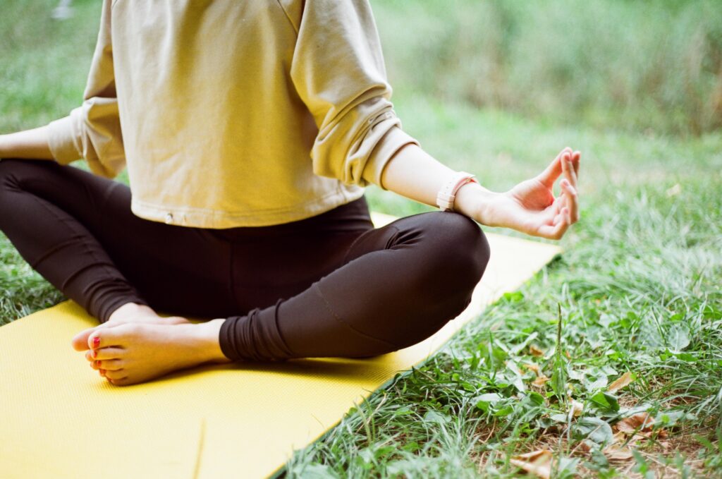 A person meditating outside on a yellow yoga mat.