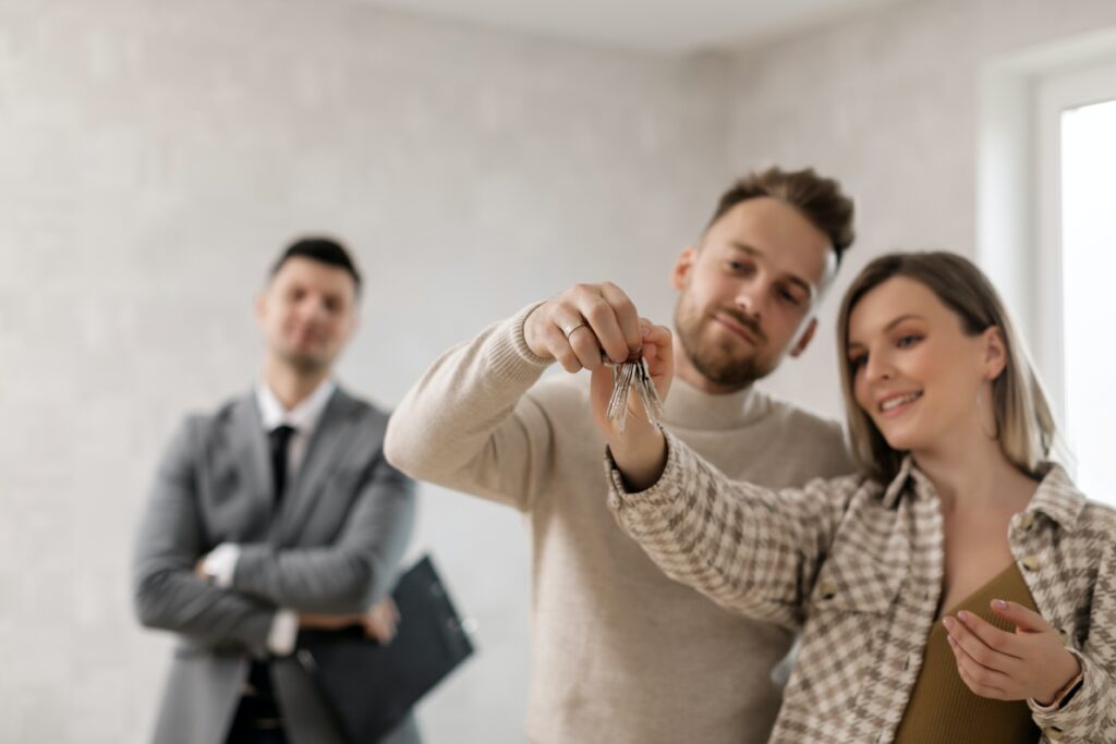 A man and woman hold the keys to their new house with the realtor smiling in the background.