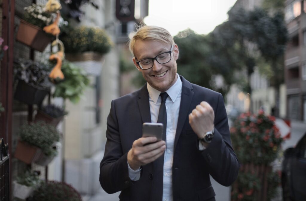 A man wearing a business suit celebrates from something on his phone.