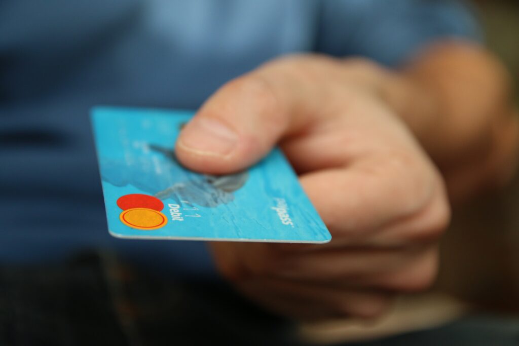 A caucasian hand holding a teal Mastercard to make a purchase.