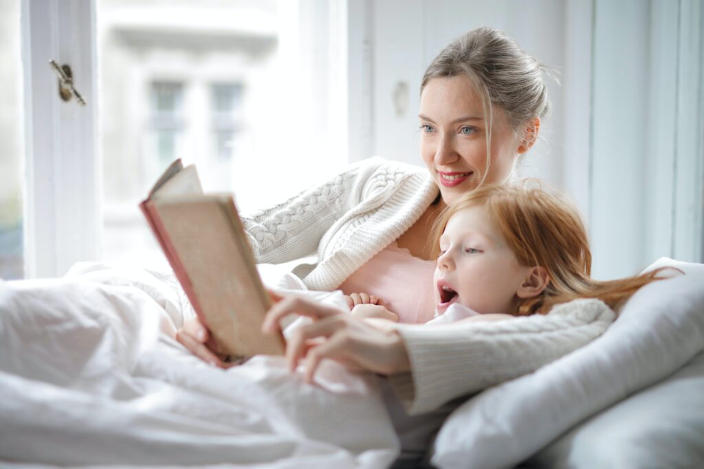 A woman lounges on a couch as she reads a story to a child.