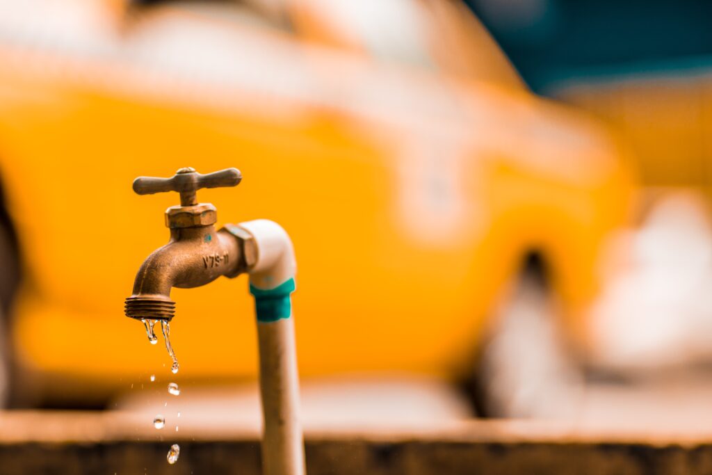A leaking water spicket in front of a yellow car.