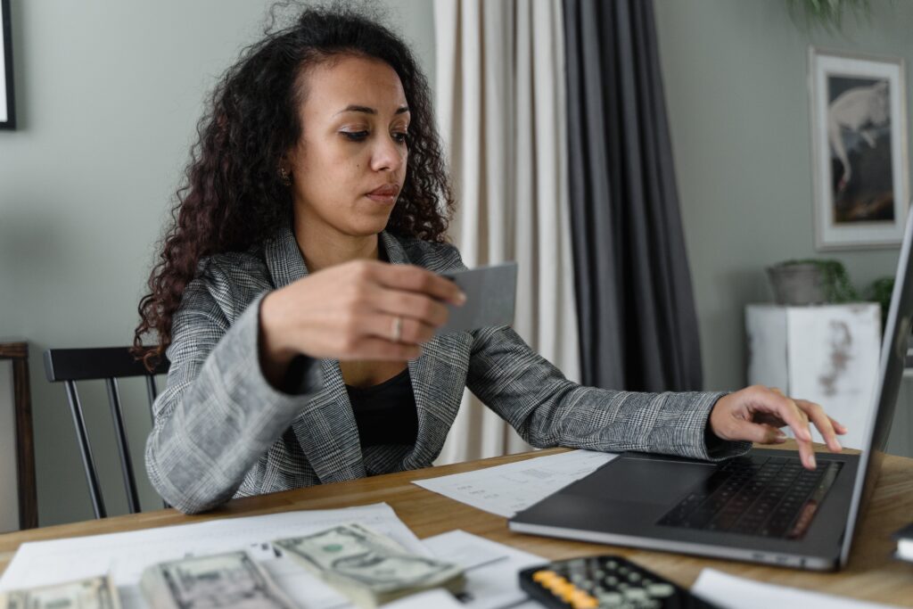 A woman sitting at a desk with piles of money as she types a credit card number into a computer.