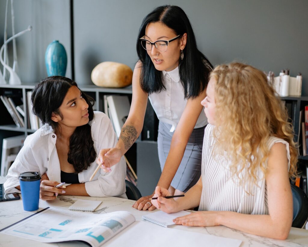 Three female business professionals collaborate over a table full of charts, graphs and other documents.