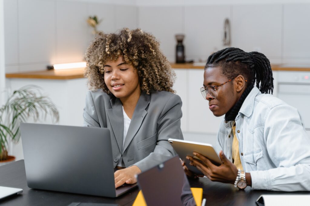 Two young professionals of color are collaborating at a desk as they peer at a computer screen.