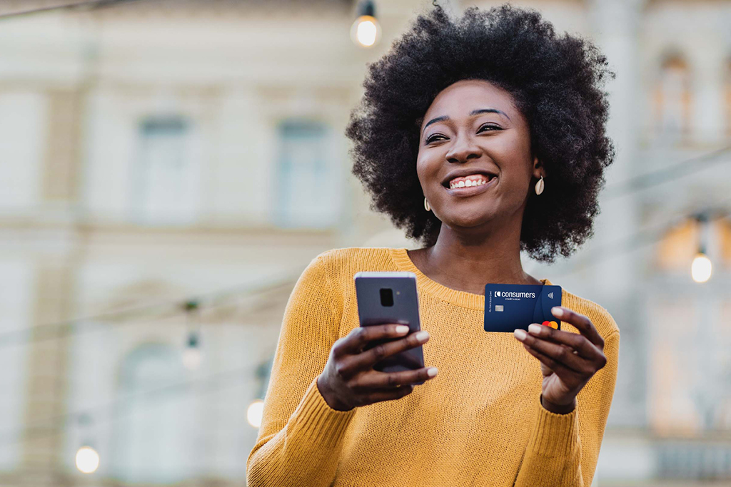 Black woman wearing yellow sweater holding her phone and a credit card