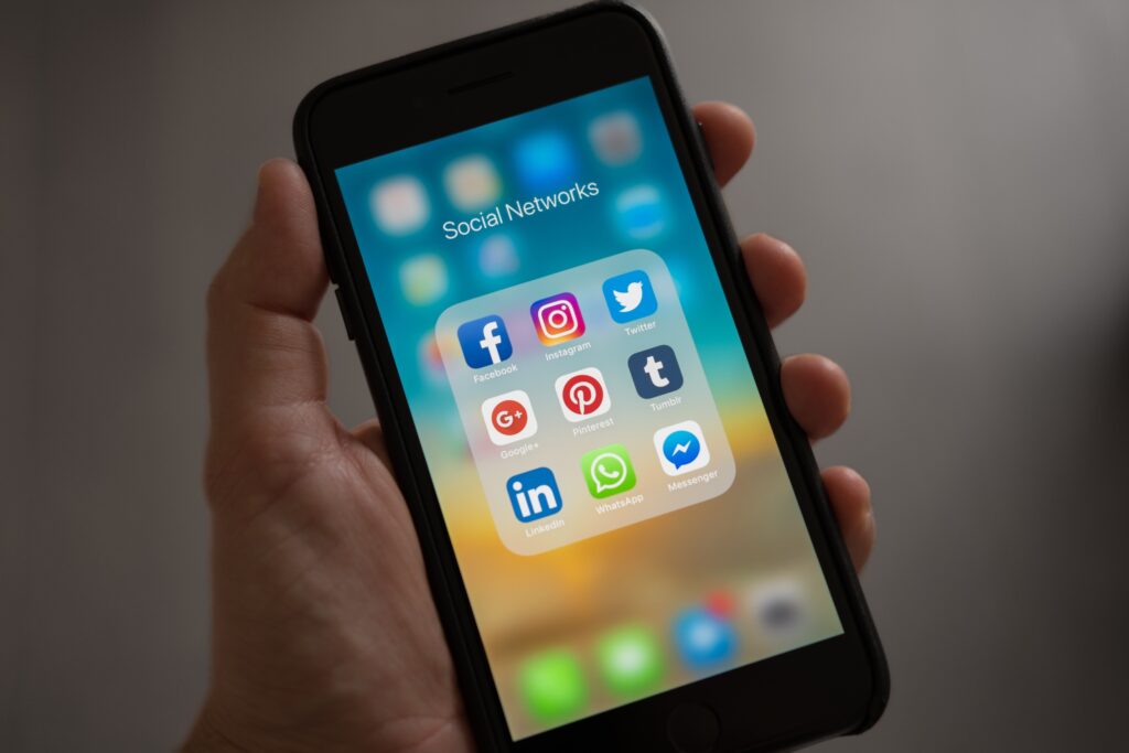 A hand holding a black iPhone displaying several social media apps, including Facebook, Instagram, Twitter and more.