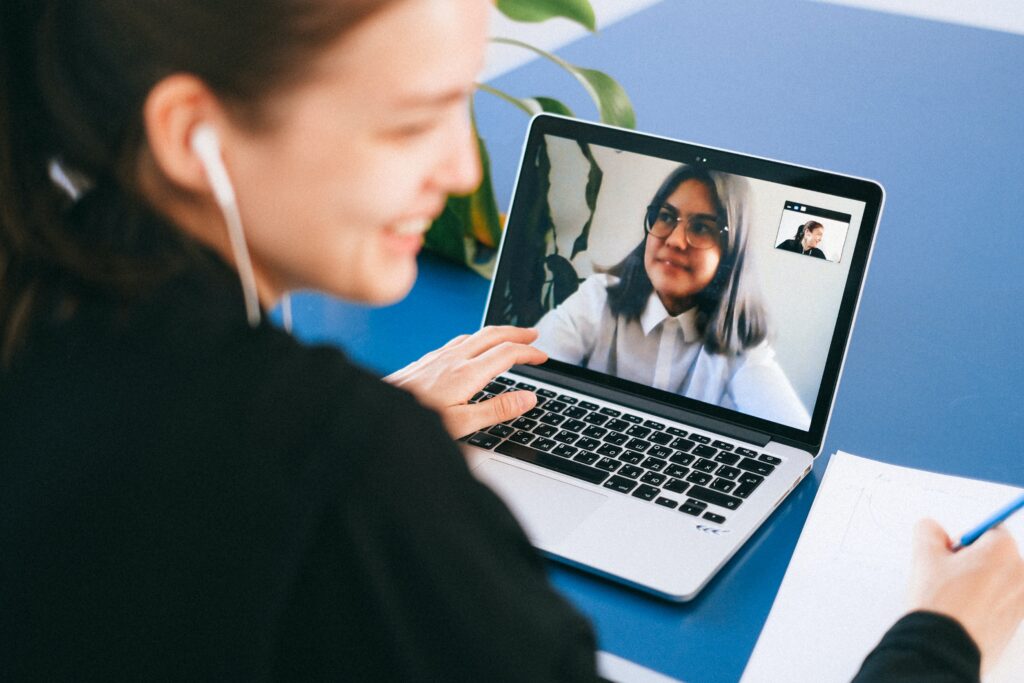 A woman sitting at a desk in front of a computer with a video meeting in progress.