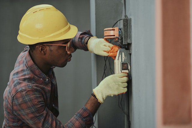 A man wearing a hard hat and other protective equipment inspects a buildings electrical system.