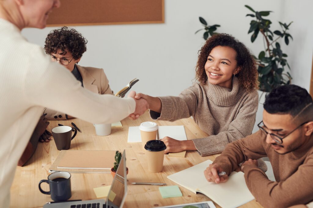 Four business professionals seated at a conference table collaborating, while two professionals shake hands.
