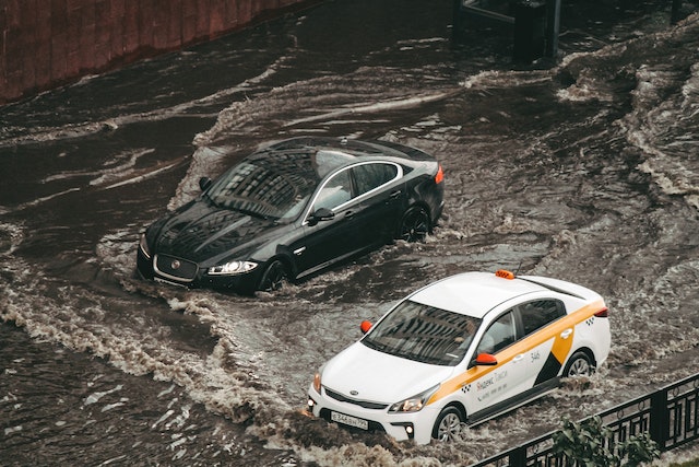 A black car and a white car sitting in a flooded road.