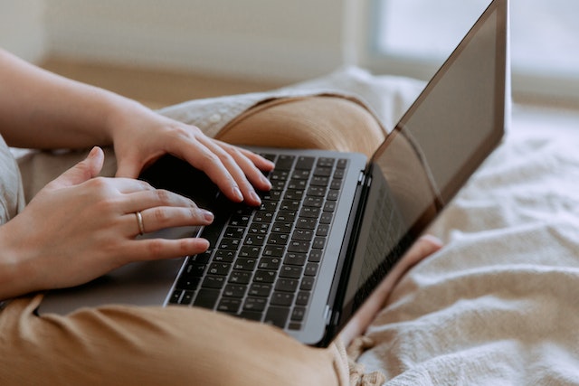 A person using a computer on their lap as they sit on the bed.