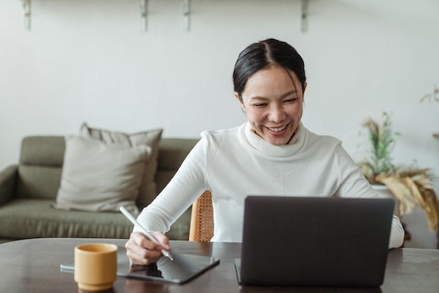 A smiling woman works at a table on a computer.