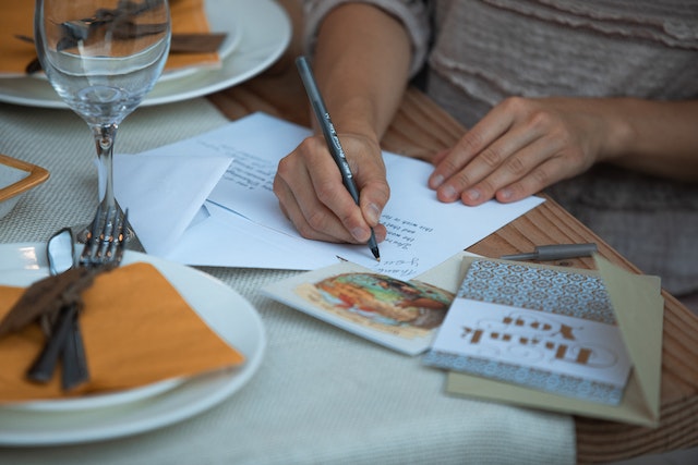 A person writing a thank you note on a table.