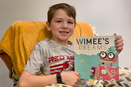 Young male child sitting in chair holding Wimee book