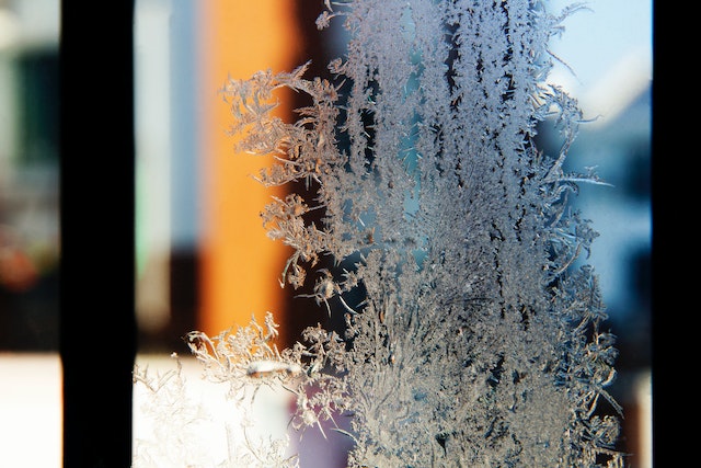 A glass window pane with frost crystals creeping across the surface.
