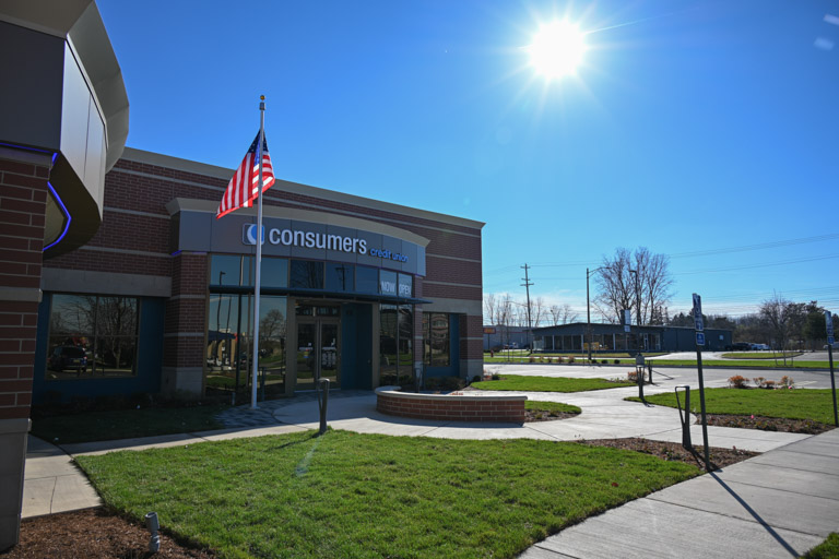 The new Cedar Consumers Credit Union office in Lansing, with the American flag in front of the building, green grass, and the sun shining in a clear blue sky.
