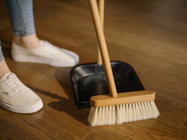 A broom sweeping a pile of dust into a dust pan on a wooden floor.