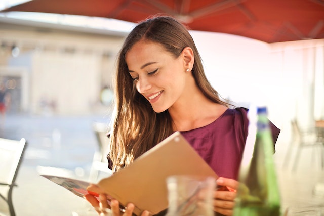 A woman sitting at a dining table in a restaurant as she reads through a menu.