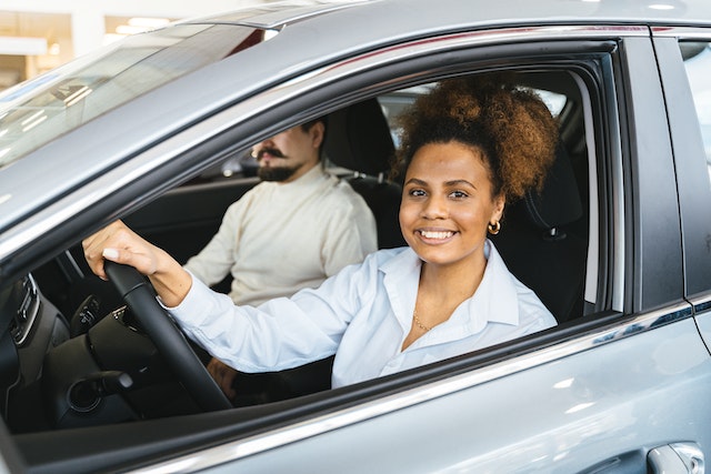 A woman smiling from the driver's seat of a vehicle with the window open.