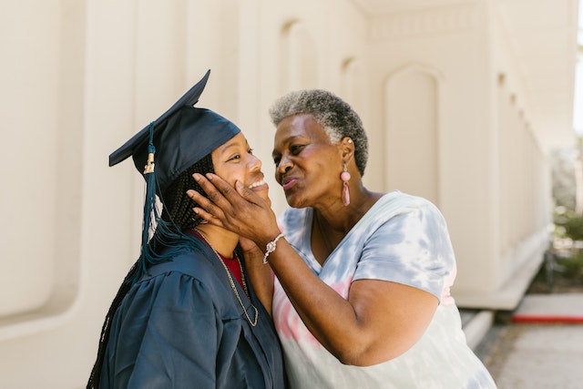 An elder woman is embracing a younger woman wearing college graduation robes.