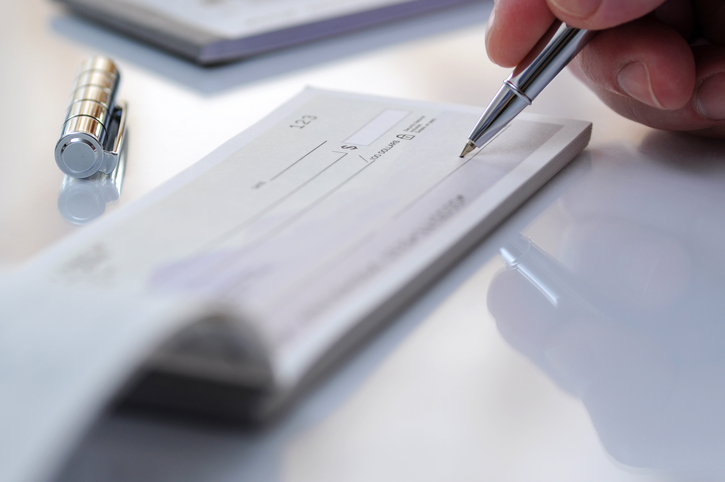 A person writing in an open checkbook with a pen.