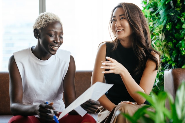 Two female business professionals smile as they converse with each other.